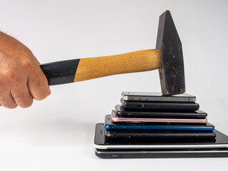 A hammer with a wooden handle breaks a stack of smartphones.