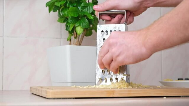A man rubs cheese on a metal grater for freezing and further cooking pizza, pasta.