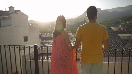 Pregnant young caucasian woman and man looking out at the town on against mountains on elevated observation deck. Couple spending time together.