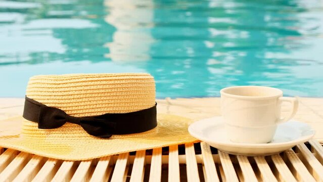  Close-up of a cup of coffee and a straw hat on the background of a blue swimming pool on a summer sunny day. Good morning concept and planning a new day, week, month. Vacation and travel. copy space
