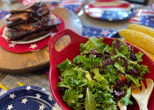 Salad in a red bowl set up on a red, white, and blue decorated table for Independence Day celebration