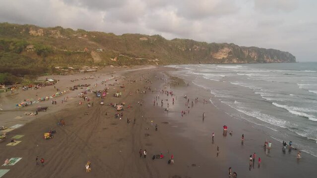 sandy beach parangtritis near ocean with big waves, people in tropical resort at sunset. Yogyakarta, Indonesia. aerial view seascape, ocean and beautiful beach. Travel concept. Indonesia, java
