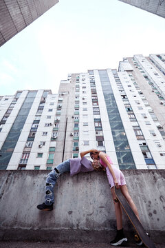 Teenage couple kissing and hugging in urban exterior surrounded by buildings.