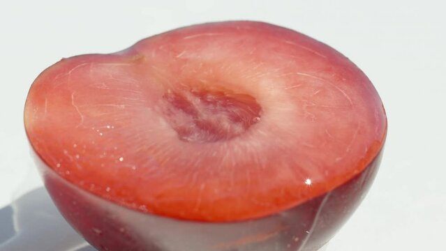 Half of a red plum is lying on a white table, water drips on it. Close-up.