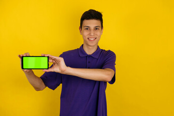 Portrait of a young man points his finger at the smartphone screen on yellow background