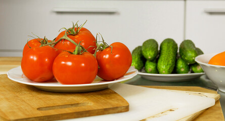 On the table are tomatoes, cucumbers, carrots, cheese, bread in a basket, herbs, dill, green onions, a knife on the board