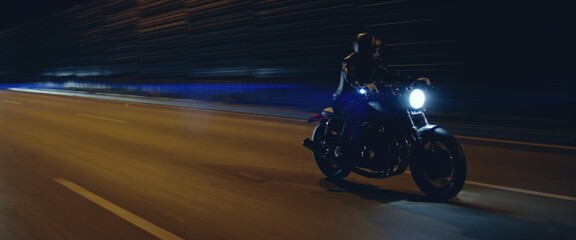Biker riding his custom built cafe racer motorcycle through city at night. Shot with 2x anamorphic...
