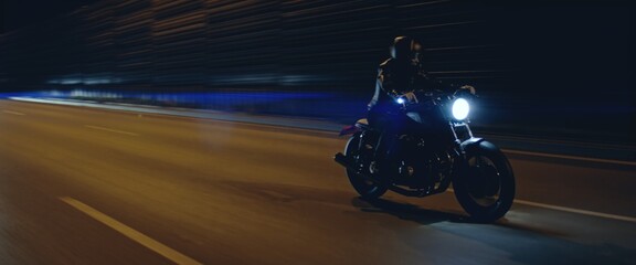Biker riding his custom built cafe racer motorcycle through city at night. Shot with 2x anamorphic lens