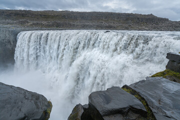 Biggest waterfall in Europe, Dettifoss. Muddy waters falling over the edge. Majestic Icelandic waterfall on a rainy, cloudy day.