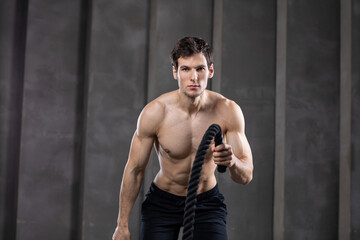 Fototapeta na wymiar Athletic young man with rope doing exercise in functional training fitness gym.