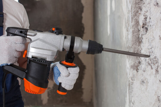 The builder is making hole in wall at construction site with hammer drill perforator equipment.