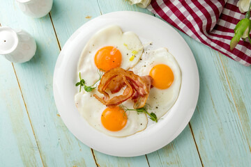 Fried eggs with bacon on white plate on wooden table top view