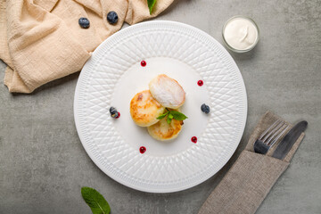 cheesecakes from cottage cheese with sour cream and fresh berries with mint on white plate top view on grey table