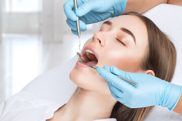 A dentist doctor treats caries on a tooth of a young beautiful woman in a dental clinic. Tooth...