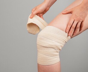 Woman wrapping elastic bandage around painful knee to relieve pain or prevent injury. Sprained...