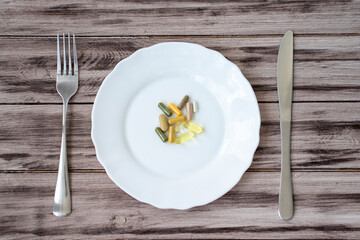 Synthetic vitamins and pills on a plate with a knife and fork on a wooden background.