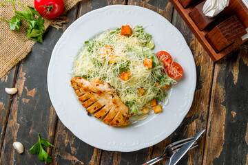 Salad caesar with chicken on white plate on old wooden table top view