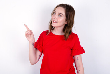 Smiling young caucasian woman wearing red T-shirt over white background indicating finger empty space showing best low prices