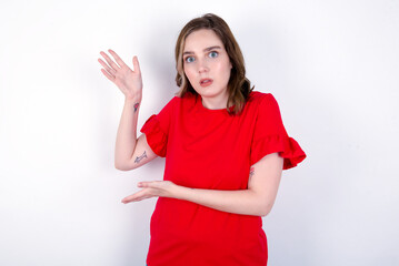 young caucasian woman wearing red T-shirt over white background pointing aside with both hands showing something strange and saying: I don't know what is this. Advertisement concept.