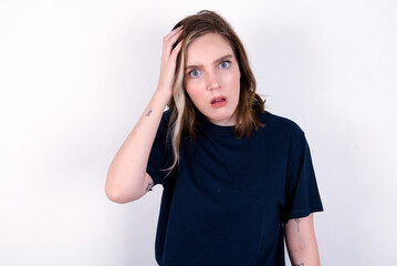 Embarrassed young caucasian woman wearing black T-shirt over white background with shocked expression, expresses great amazement, Puzzled model poses indoor