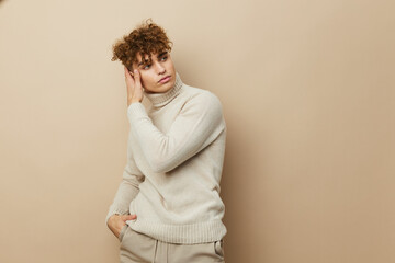 a handsome, attractive man stands on a beige background in stylish clothes and holding his hand near his face in a relaxed manner