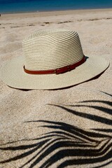 Fototapeta na wymiar wicker hat and shadow from a palm tree on the sand