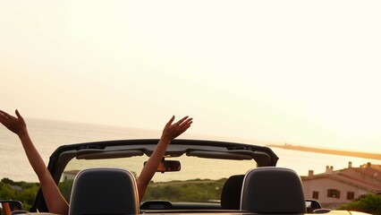 Lonely woman in a black convertible car looks at the sunset in front of the sea and is moved by how...