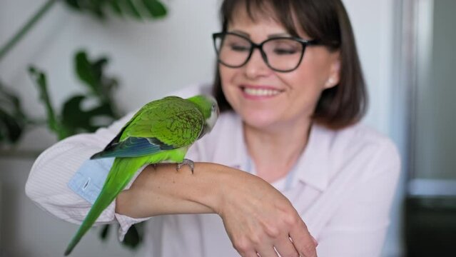 Mature woman at home with a pet parrot on her arm