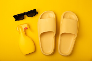 Flat lay composition with beach accessories on yellow background. Beach slippers, sunglasses and sunscreen.SPF sun protection.Space for copy.Place for text.Vacation concept.