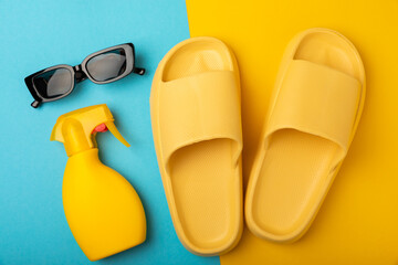 Flat lay composition with beach accessories on yellow background. Beach slippers, sunglasses and sunscreen.SPF sun protection.Space for copy.Place for text.Vacation concept.