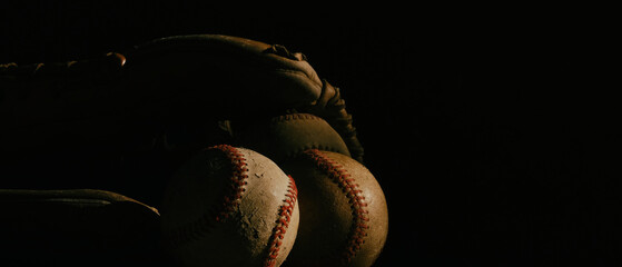 Worn used baseball balls with vintage glove on dark background with copy space