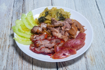 Pork Leg Stew, Red Pork, Crispy Pork and Chinese Sausage served with pickled lettuce and cucumber in a white plate.