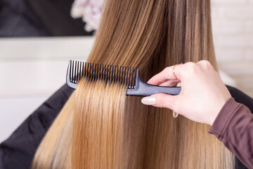 Hairdresser's hand brushing long natural blonde hair in beauty salon