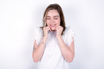 young caucasian woman wearing white T-shirt over white background grins joyfully, imagines something pleasant, copy space. Pleasant emotions concept.