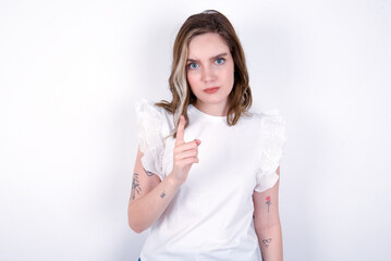 young caucasian woman wearing white T-shirt over white background frustrated and pointing to the front