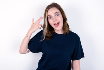 Obraz na płótnie Canvas young caucasian woman wearing black T-shirt over white background foolishness around shoots in temple with fingers makes suicide gesture. Funny model makes finger gun pistol