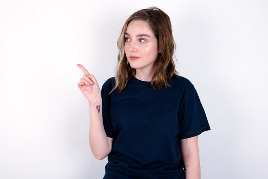 young caucasian woman wearing black T-shirt over white background points at copy space and advertises something, advices best price.