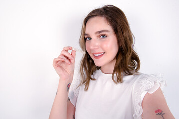young caucasian woman wearing white T-shirt over white background make selfie holding an invisible braces aligner, recommending this new treatment. Dental healthcare concept.