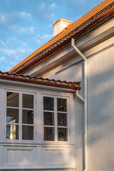 Bottom - up view of tiled roof of white building with blue sky in the background on a sunny summer day.