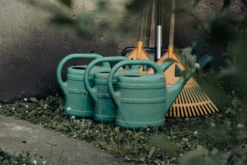 Close-up of plastic watering cans and leaf rakes placed against a concrete wall.