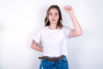 young caucasian woman wearing white T-shirt over white background feeling serious, strong and...