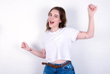 young caucasian woman wearing white T-shirt over white background , dancing and listening music with headphones.