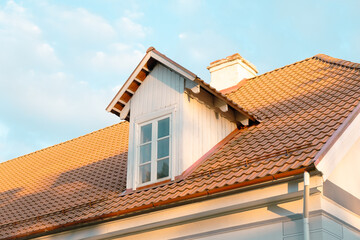 Bottom - up view of tiled roof of white building with blue sky in the background on a sunny summer day.