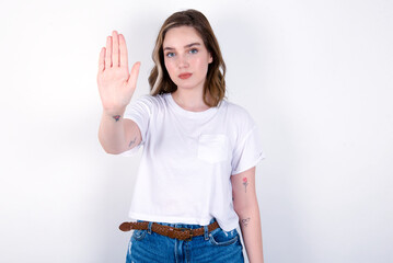 young caucasian woman wearing white T-shirt over white background doing stop gesture with palm of...