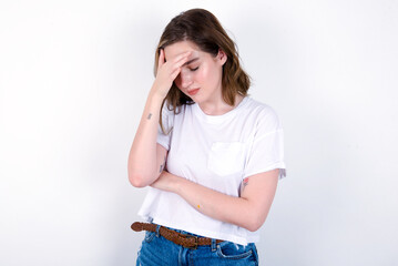 young caucasian woman wearing white T-shirt over white background making facepalm gesture while smiling amazed with stupid situation.