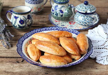Homemade small pies with stuffing on a platter, on a wooden table. Rustic style, selective focus.