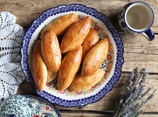 Homemade small pies with stuffing on a platter, on a wooden table. Rustic style, selective focus.