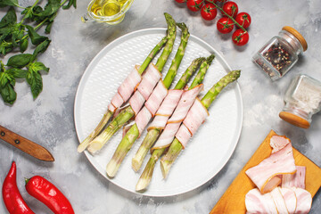 Fresh green asparagus wrapped in bacon on grey concrete table. Top view