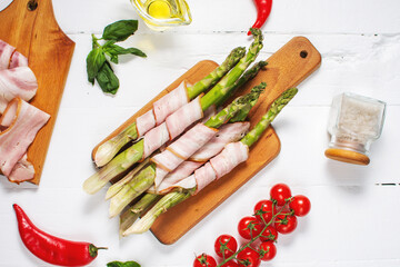 Fresh green asparagus wrapped in bacon on white wooden table. Top view