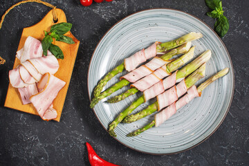 Fresh green asparagus wrapped in bacon on black stone table. Top view